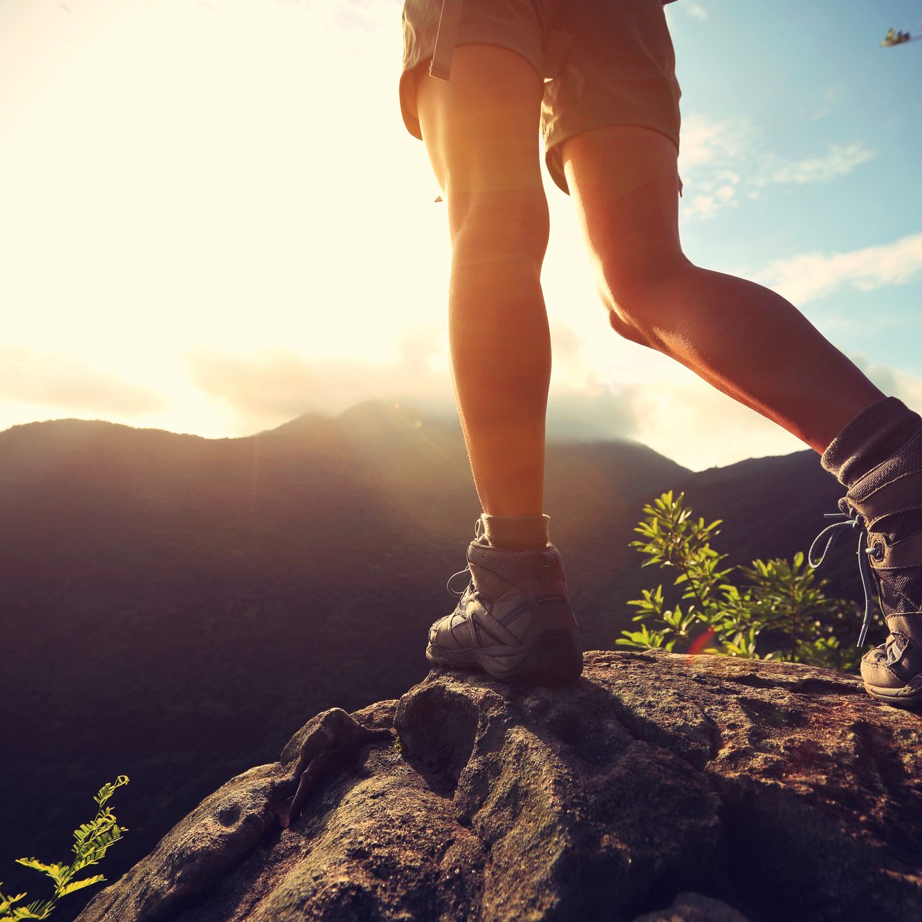 young woman hiker legs on sunrise mountain peak rock vandring med vandrestøvler